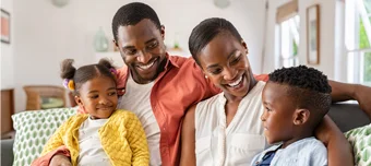 Casal feliz com filhos, sorrindo, sentados no sofá.